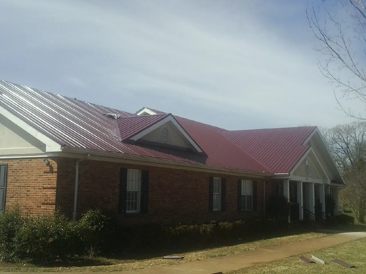 Red metal roof with gabled entries on a long brick building, from a Hail Damage Roof Repair job in Wheatland